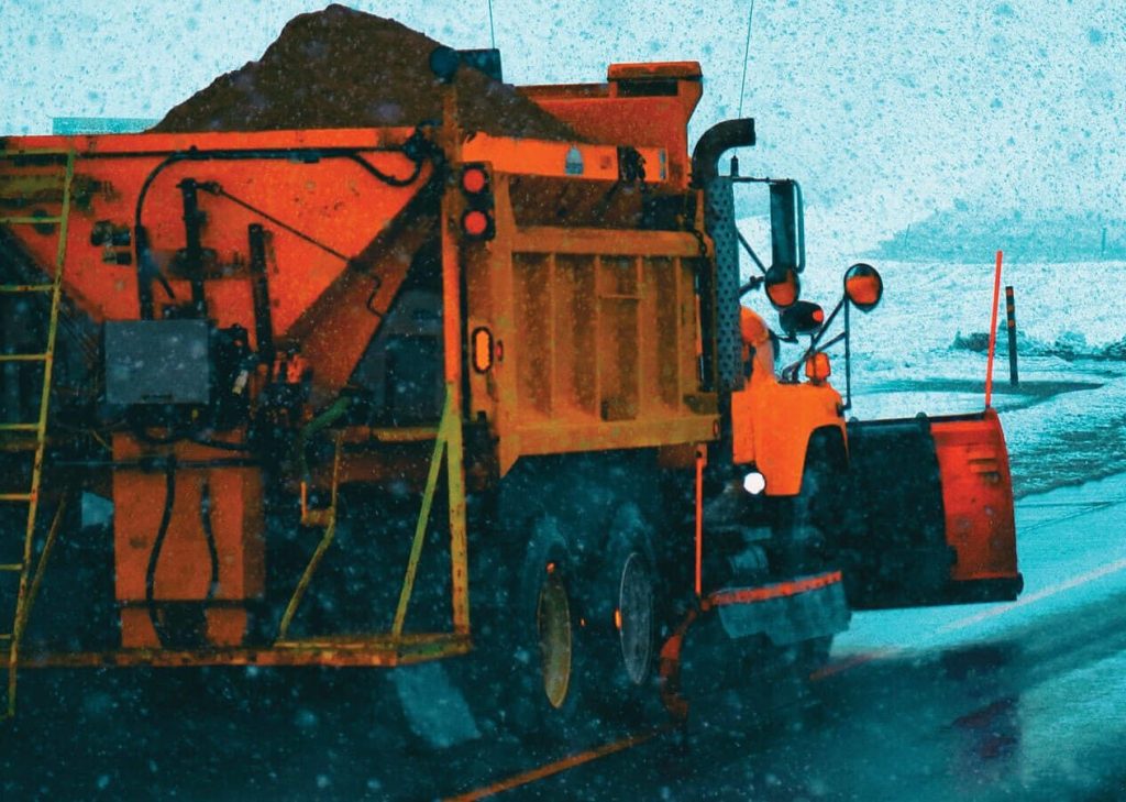 A snow plow truck driving down a snowy road.