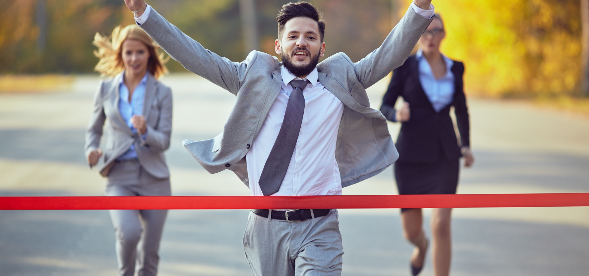 Businessman running through the finish line before the two women running behind him