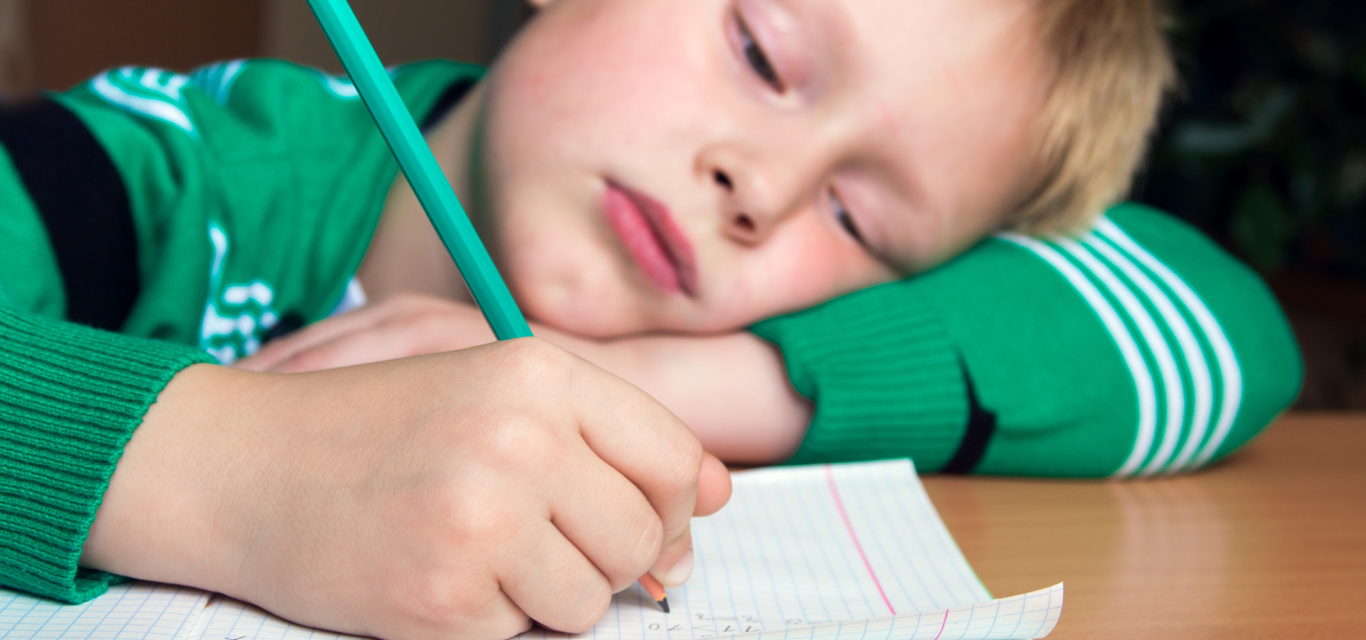 Young boy with head on the table writing on paper with a pencil