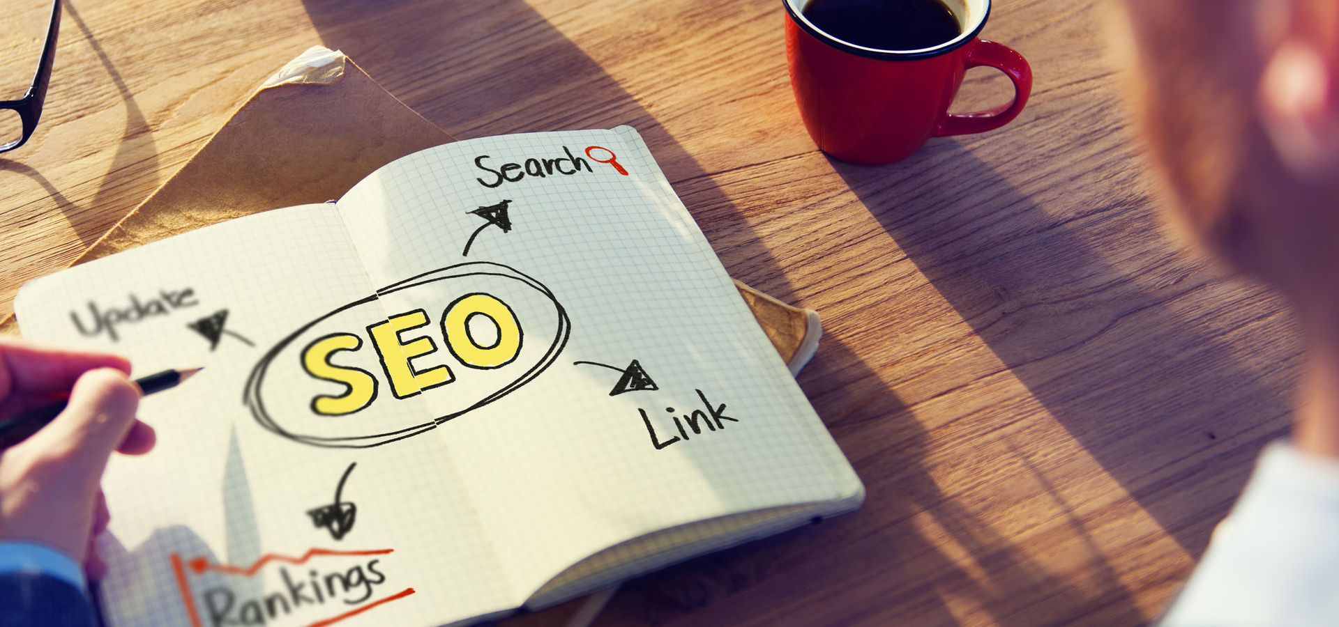 Hand with pencil writing SEO concepts on notepad