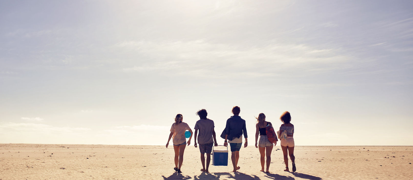 Rear view of young people carrying cooler walking on the beach