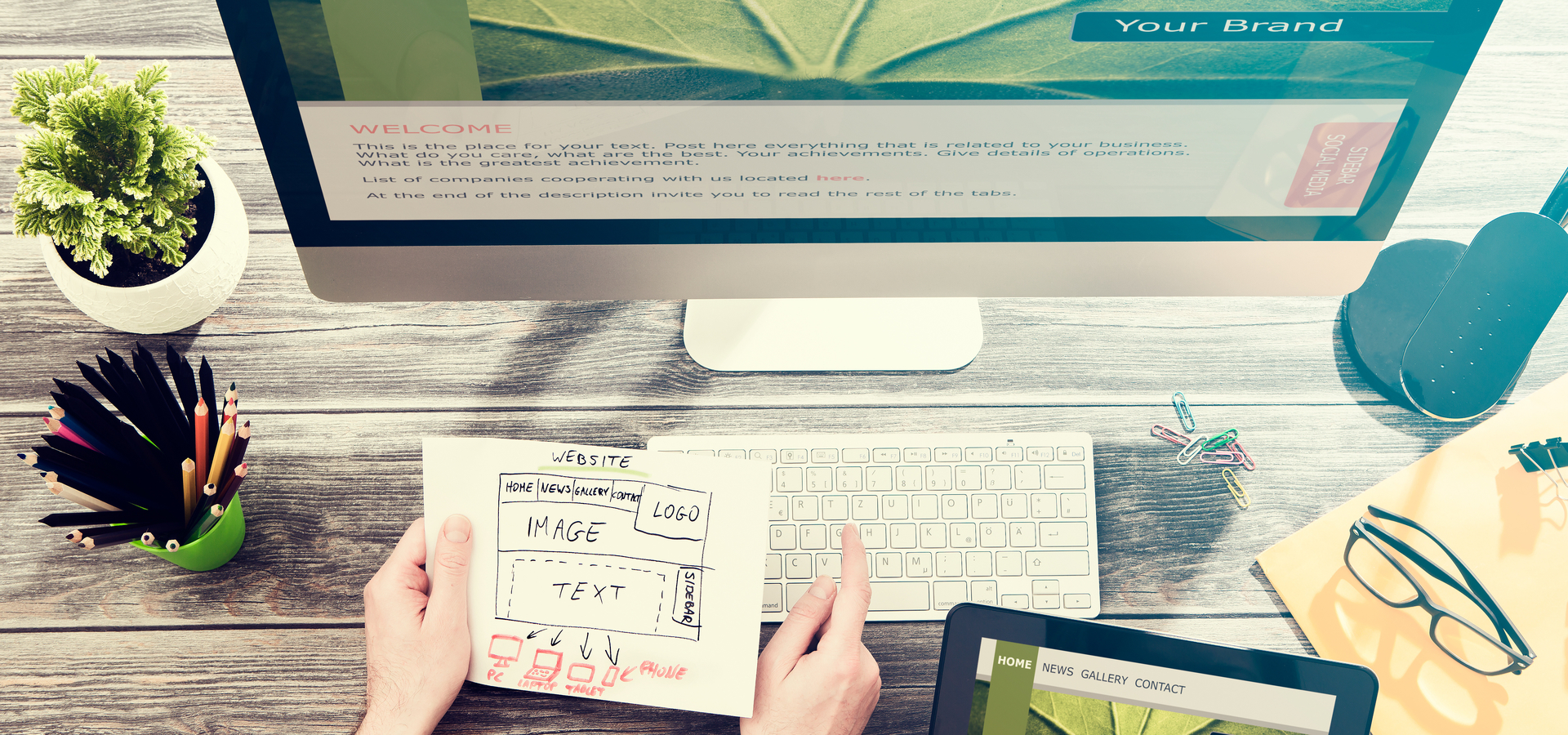 Topview of hands holding a website wireframe illustration in front of a desktop computer