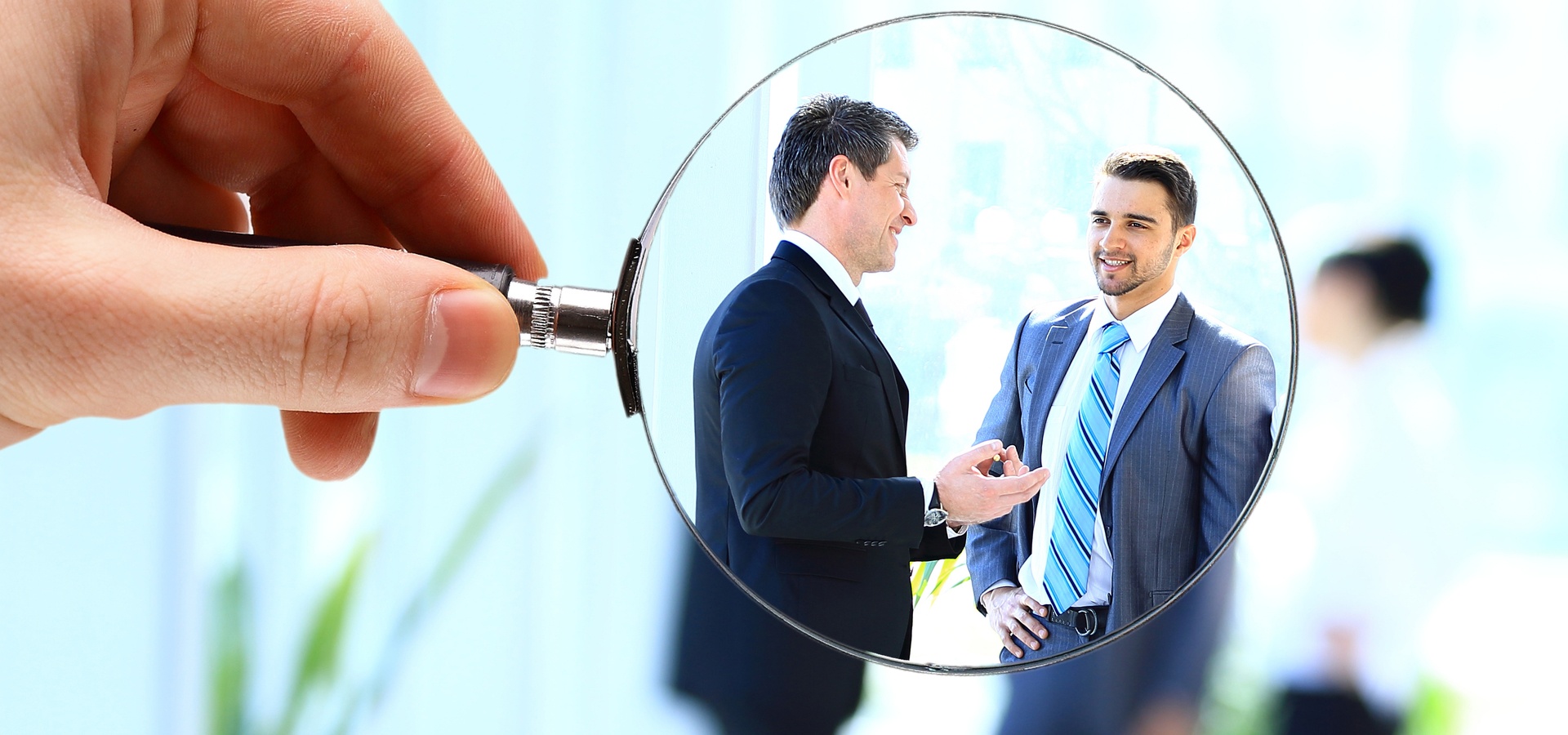 Top view of a hand holding a magnifying glass over two businessmen speaking