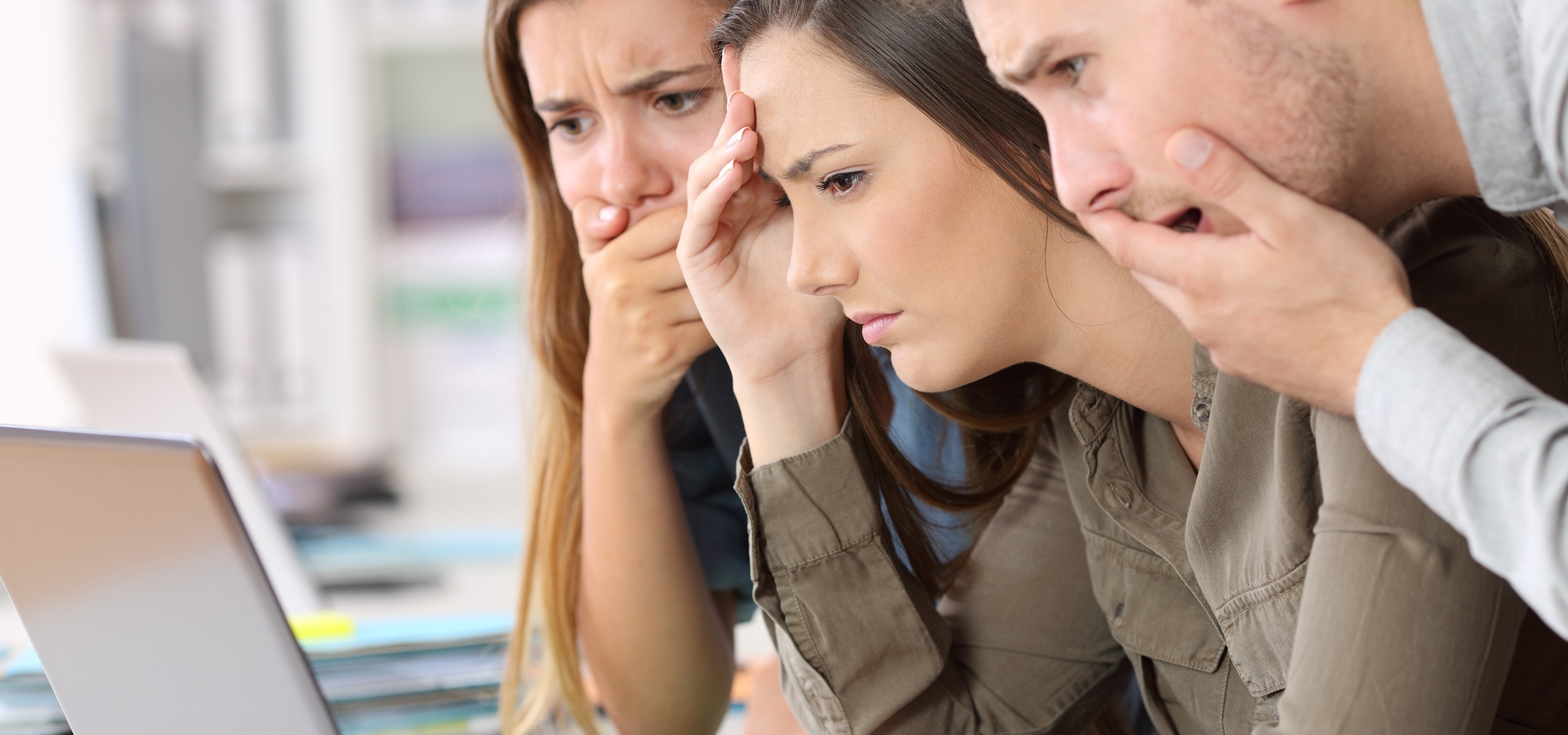 Three people looking at laptop screen looking worried