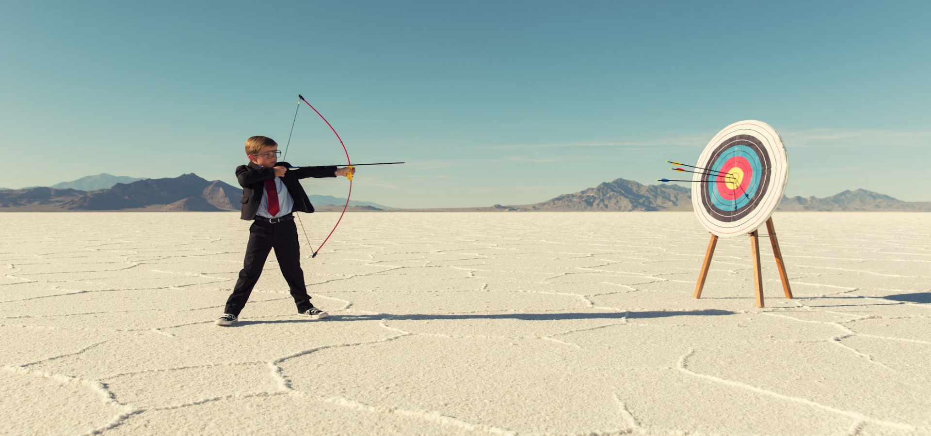 Young boy shooting a bow and arrow at a target in the desert