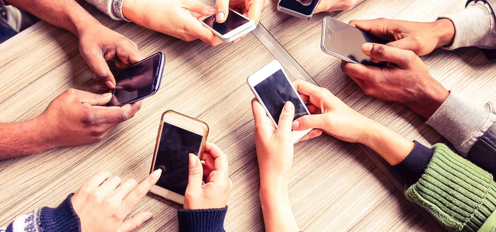 Top view of six people's hands in a circle using smart phones
