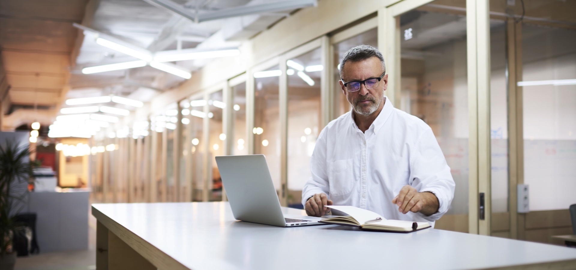 Male flipping through notebook in front of laptop in office
