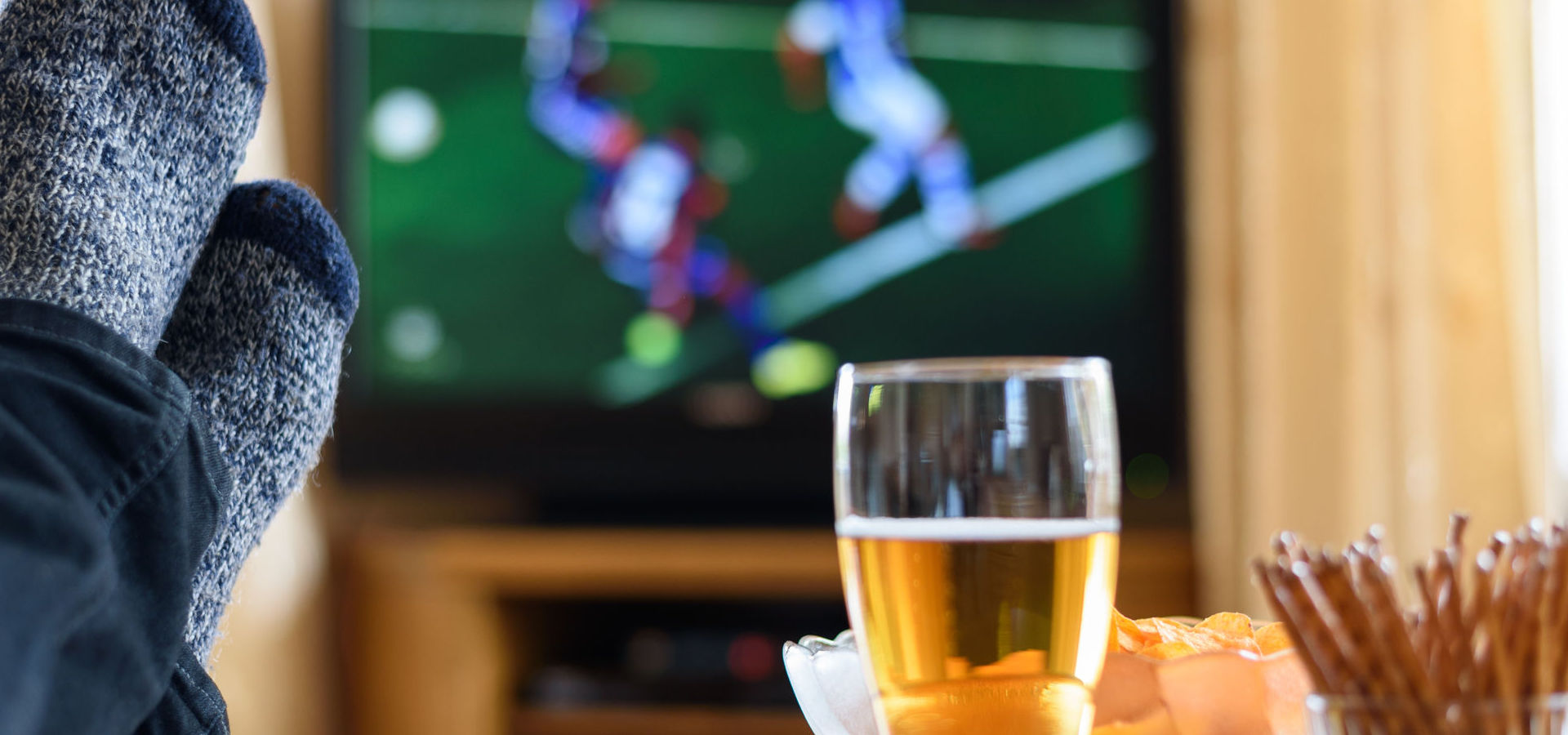 Watching a football game on TV with feet and snacks on a table
